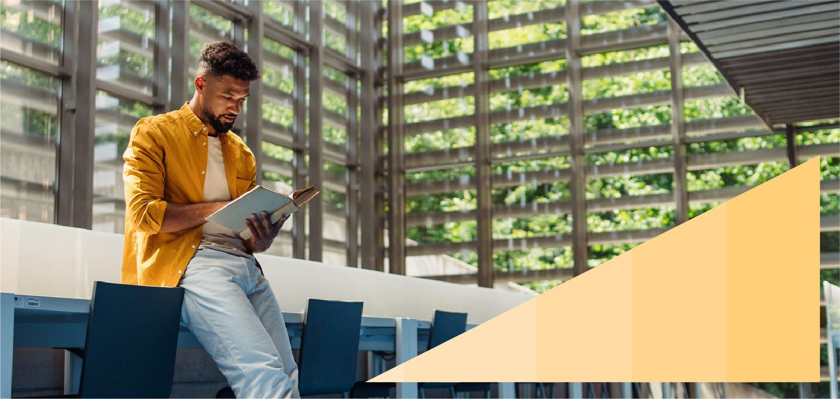 Young Black professional reading a book in a large naturally lit office lobby.