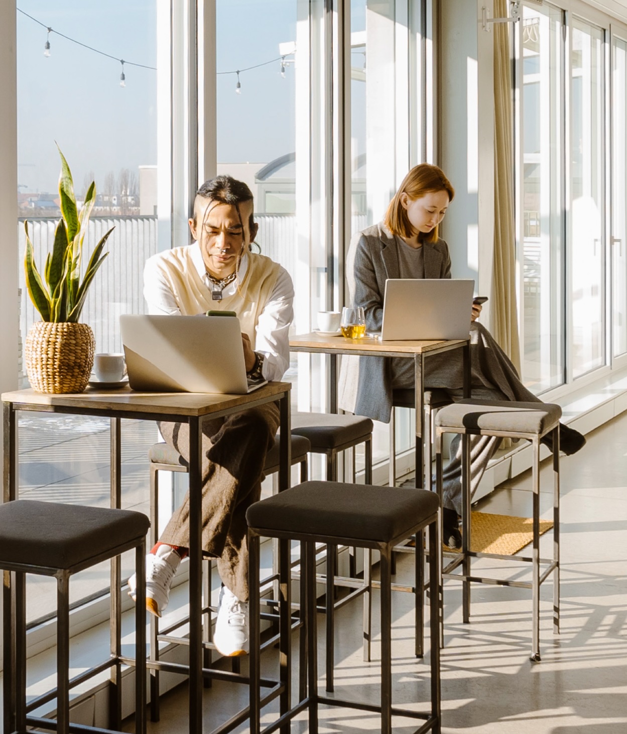 Man and woman use their cell phones in front of their open laptops at a cafe.
