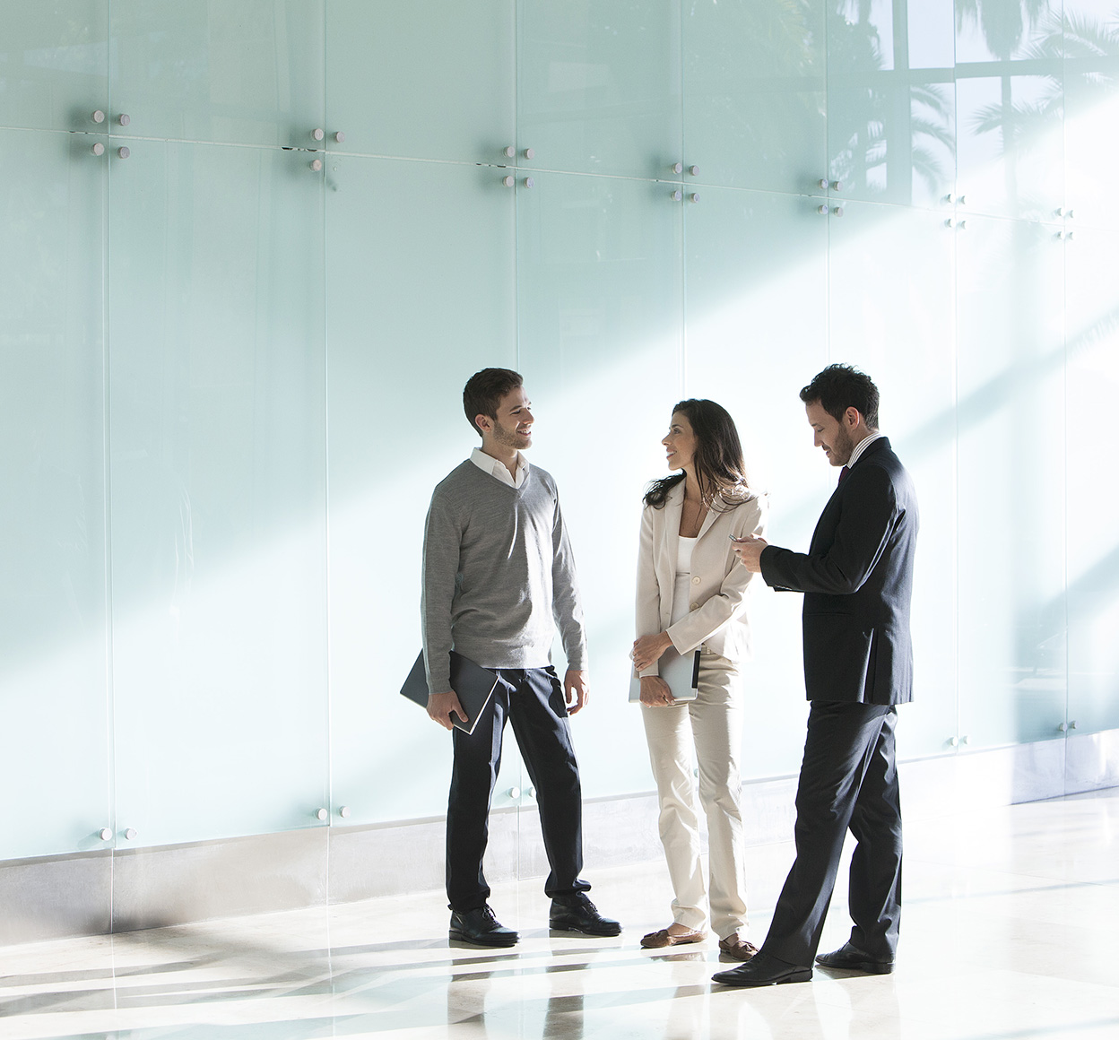 Three associates in business attire have a discussion huddled outside a conference room.